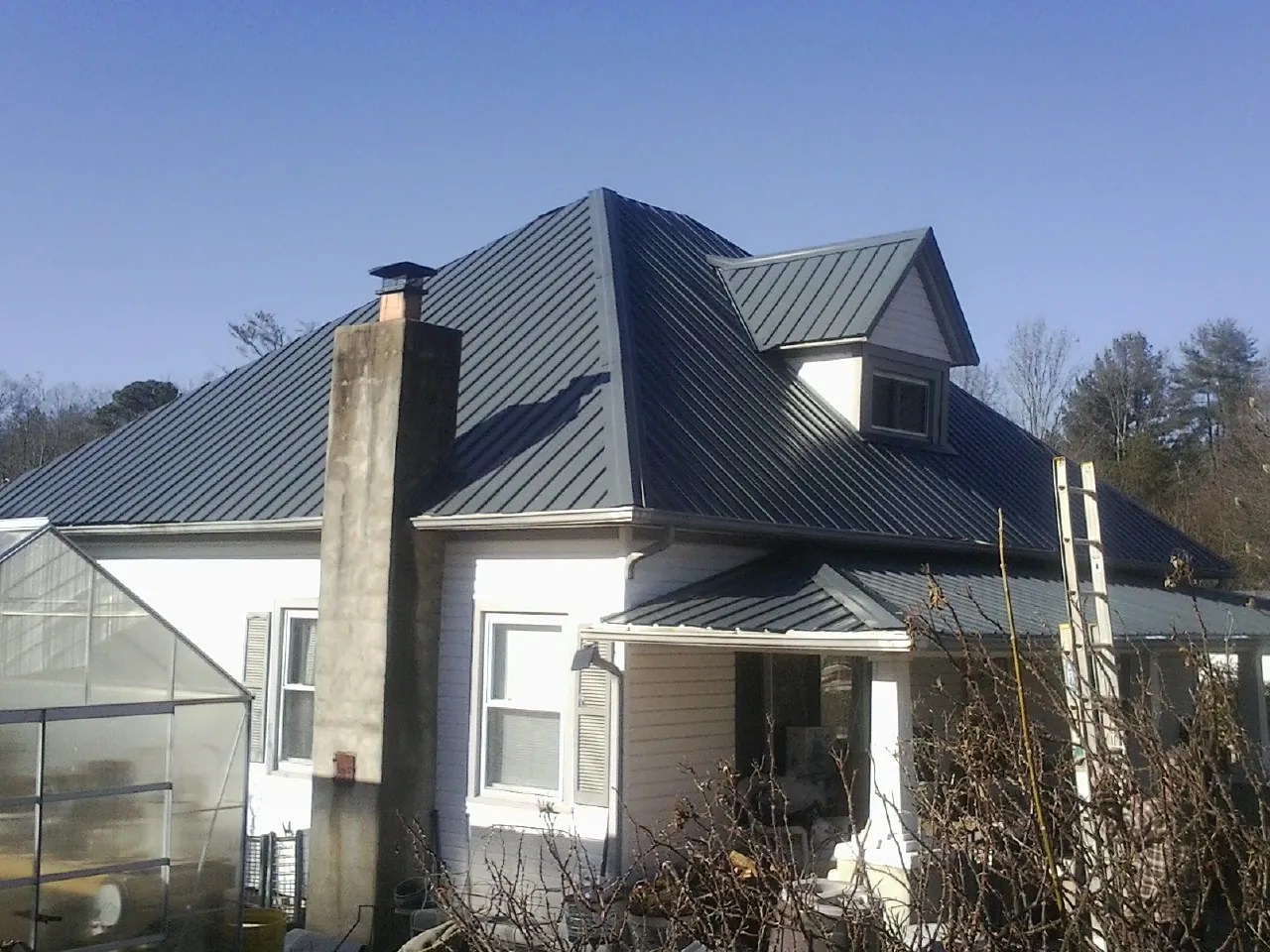 Dark blue standing seam metal roof on a white farmhouse with dormer — Slate & Tile Roof Repair by Roofing Brothers in Hot Sulphur Springs