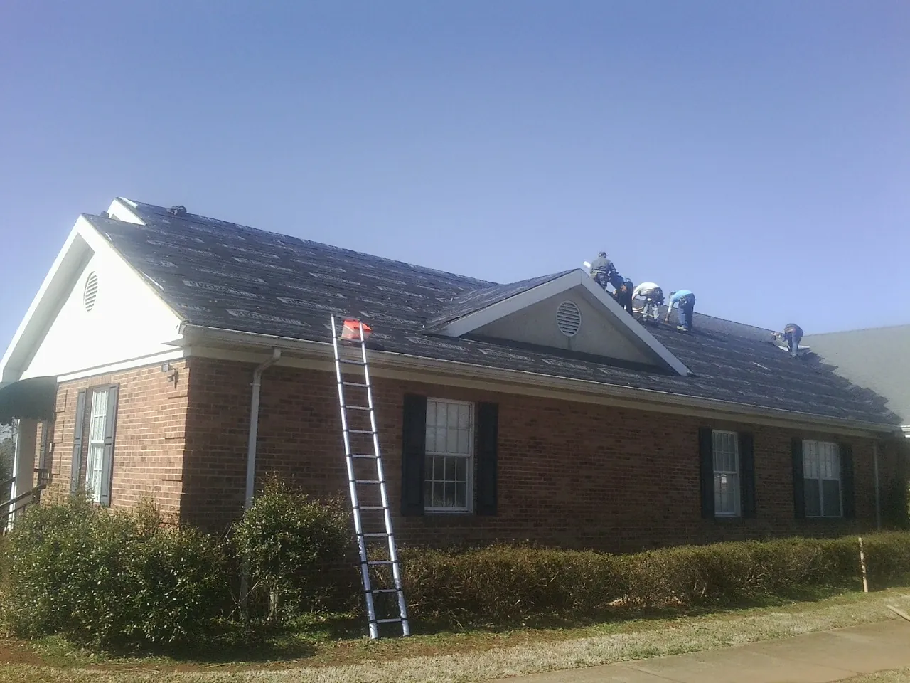 Crew tearing shingles off a brick ranch roof with a ladder set — Metal Roof Repair work by our crew in Hot Sulphur Springs