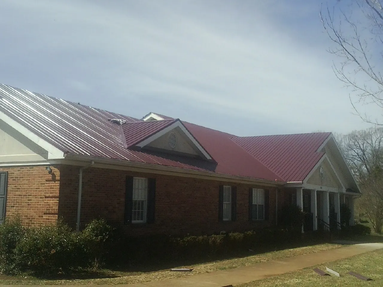 Red metal roof with gabled entries on a long brick building, from a Hail Damage Roof Repair job in Hot Sulphur Springs