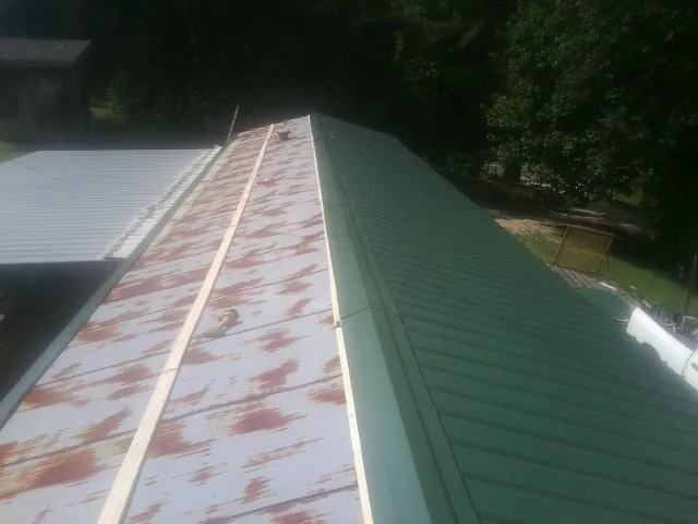 Old rusted panels beside newly installed green metal roofing — Wind Damage Roof Repair by Roofing Brothers in Hot Sulphur Springs