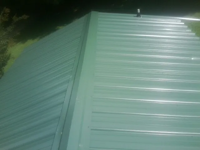 New green metal panels meeting at the ridge of a roof — Flat Roof Repair work by our crew in Hot Sulphur Springs