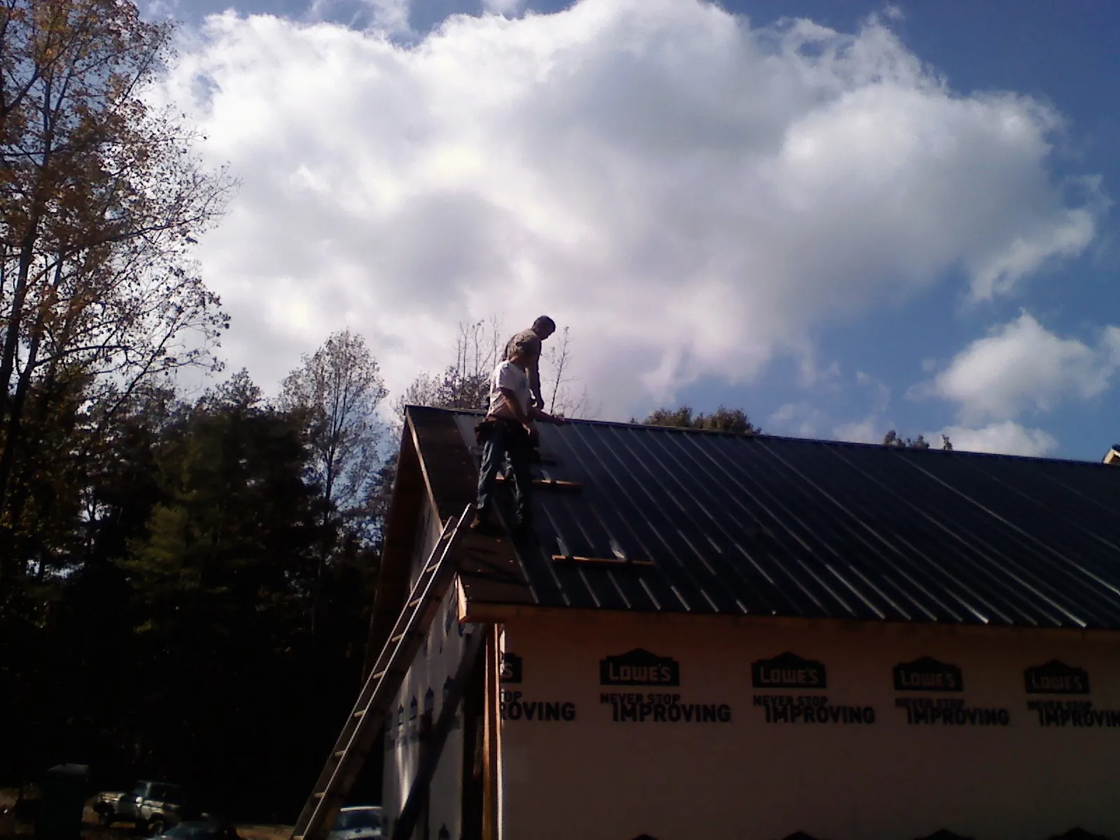 Roofer fastening dark metal panels high against a cloudy sky, from a Roof Inspection job in Hot Sulphur Springs