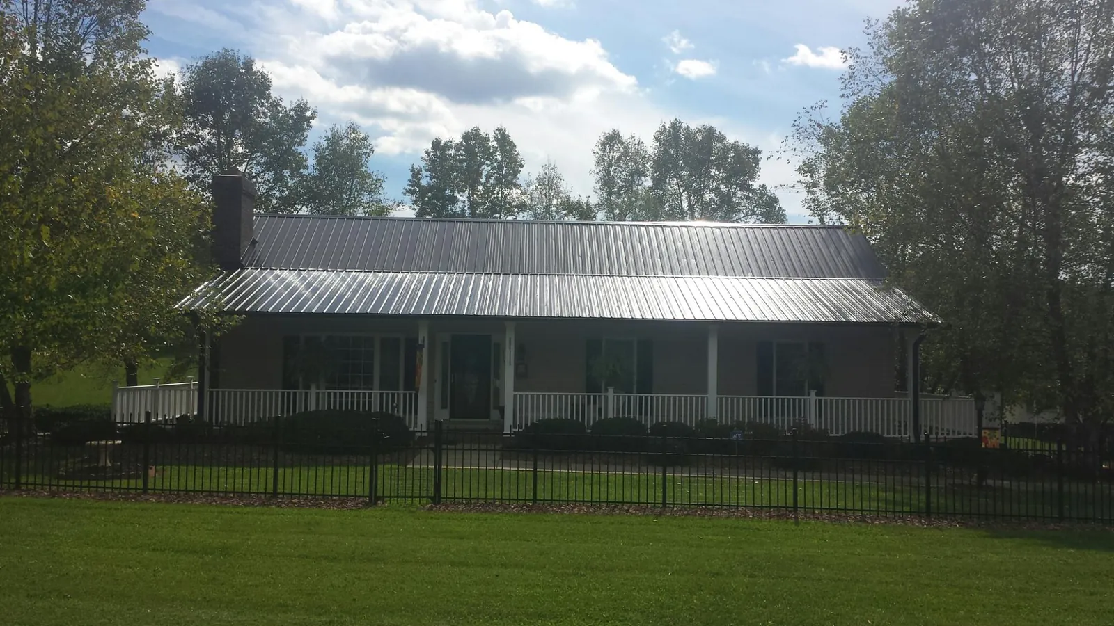 Gray metal roof on a brick ranch with a full width front porch — Gutter Guard Installation work by our crew in Hot Sulphur Springs