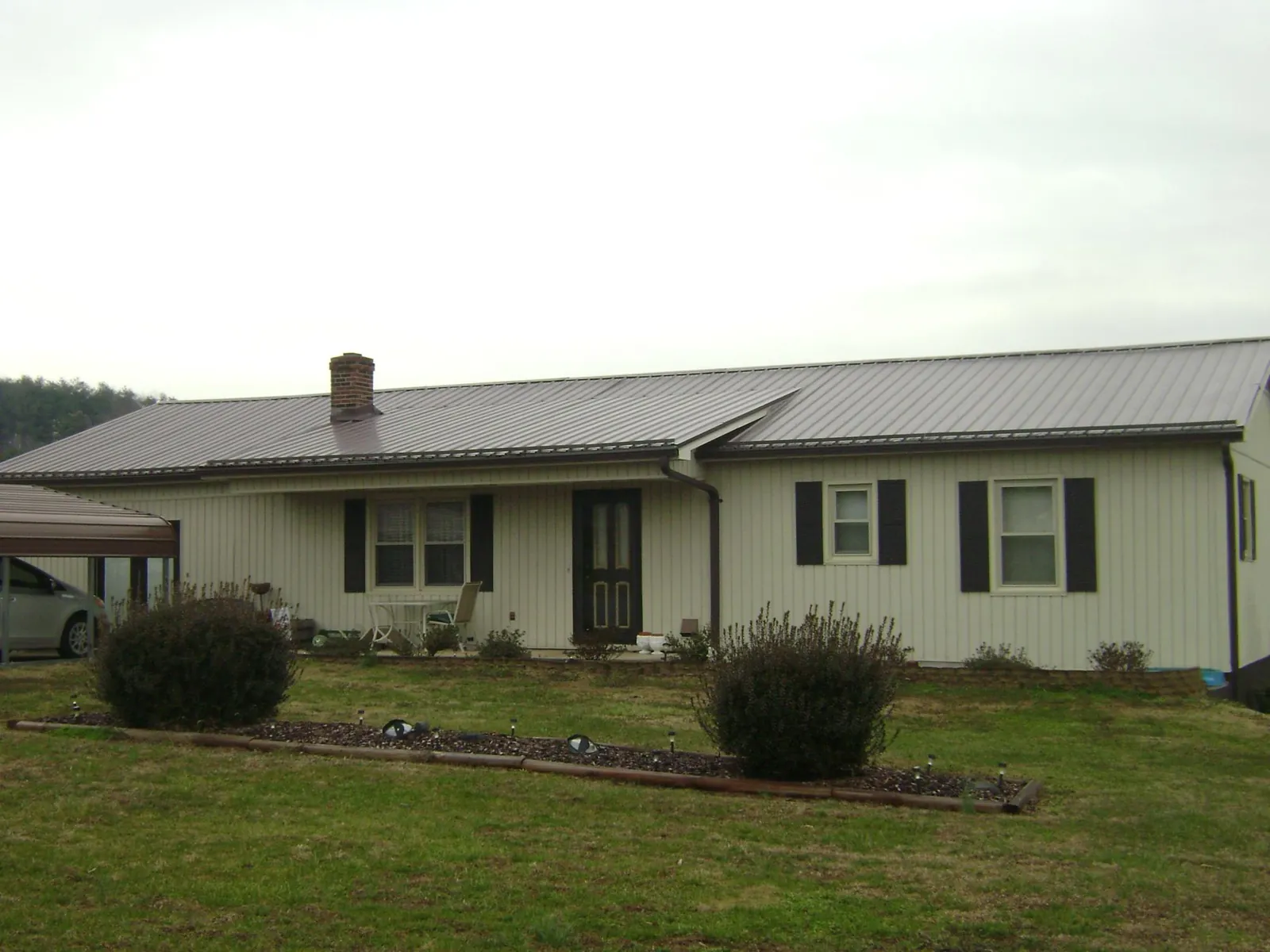 Brown metal roof on a cream sided ranch home with a brick chimney in Hot Sulphur Springs