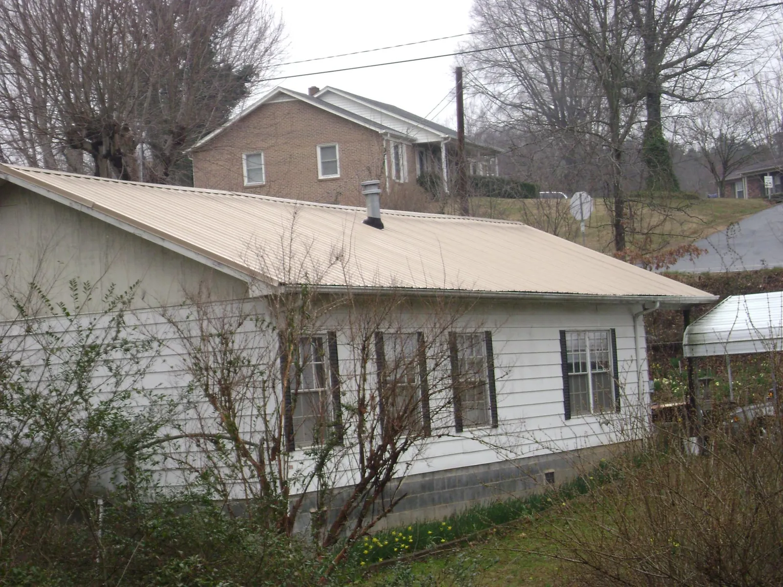 Tan metal roof on a white sided house set into a hillside — Commercial Roofing by Roofing Brothers in Hot Sulphur Springs
